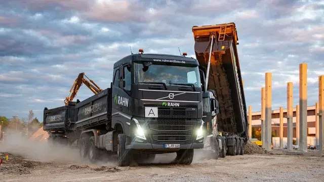 RAHN Erdbau Bagger lädt Schüttgut in Mulde bei Sonnenuntergang